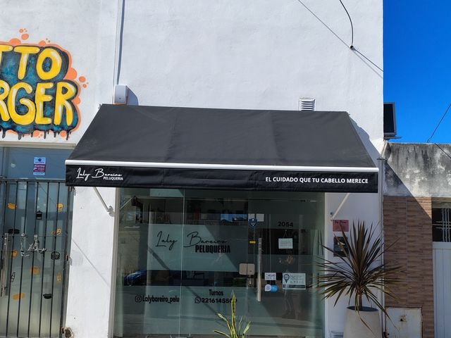 Toldo punto recto negro con el nombre del local en el frente de una peluquería