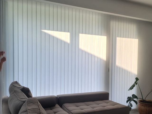 Bandas verticales blancas cubriendo el ventanal de un living con sillón