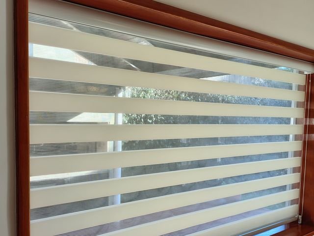 Cortina Dubai de bandas horizontales en una ventana con marco de madera