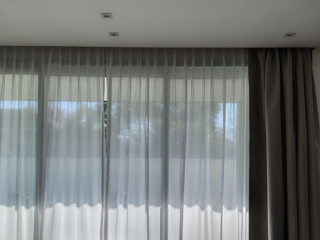 Cortinado de voile blanco con cortina gris en el living de una casa