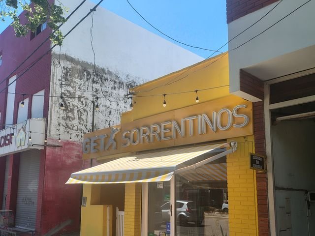 Toldo punto recto amarillo y blanco en el frente de un local de sorrentinos
