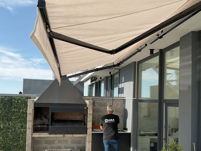 Toldo con brazo invisible color arena sobre un quincho con parrilla