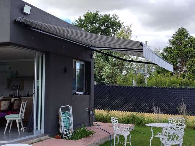 Toldo con brazo invisible de lona rayada sobre la galería de una casa con pileta