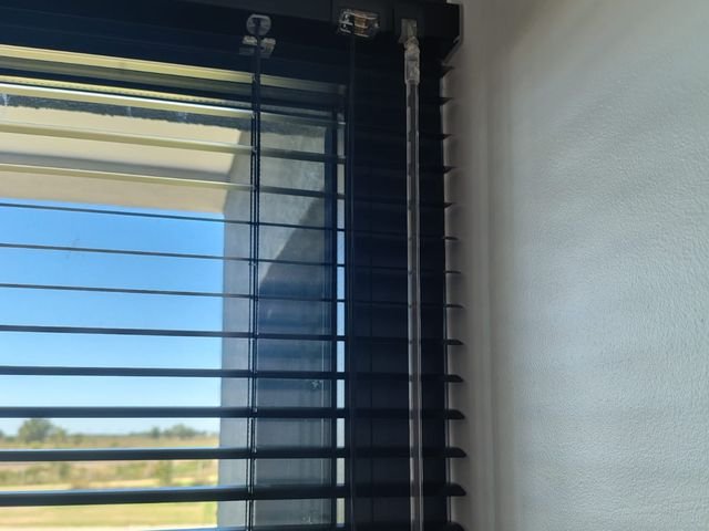 Veneciana de aluminio negra en un ventanal con vista al campo