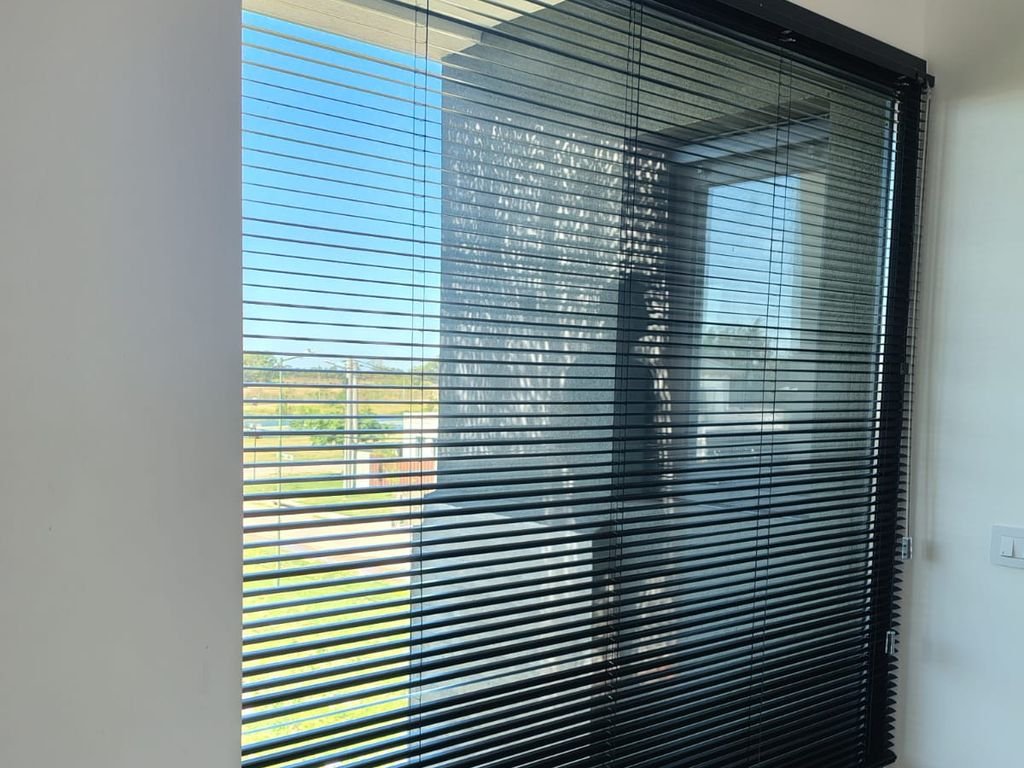 Veneciana de aluminio negra en una ventana con vista al campo